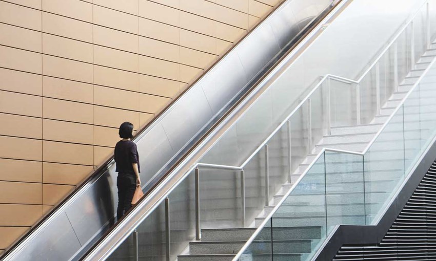 Woman standing on an escalator close to a set of stairs. Concept choosing the fastest route