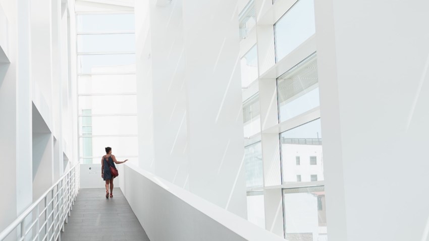 Persona che cammina in un corridoio moderno e luminoso con grandi finestre di vetro.