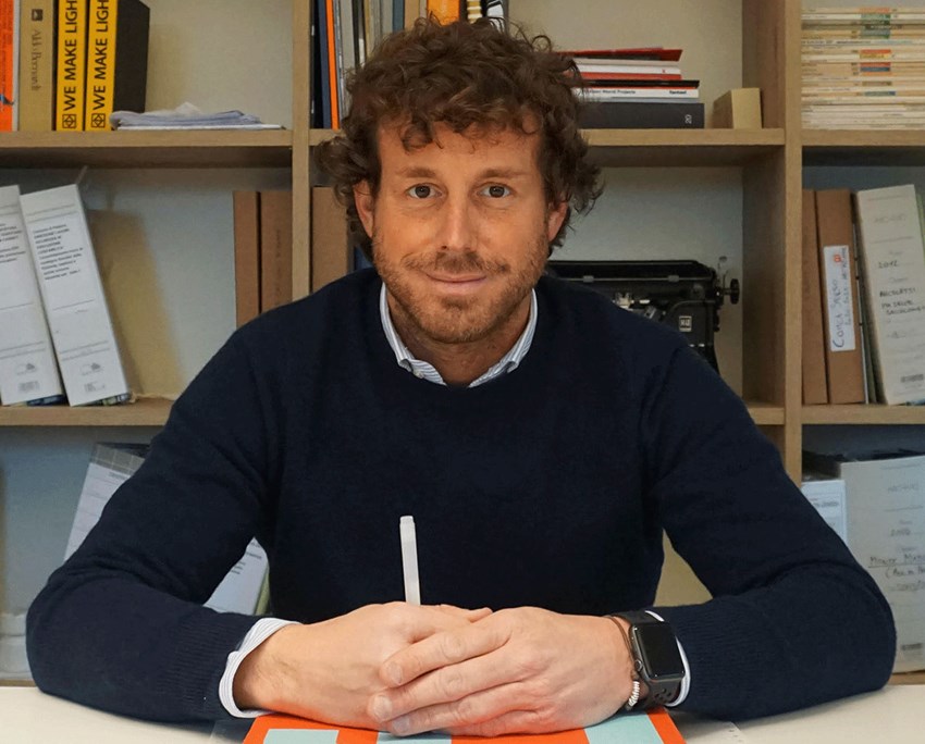 Architetto Tommaso Tommasi sorridente seduto alla scrivania con penna in mano