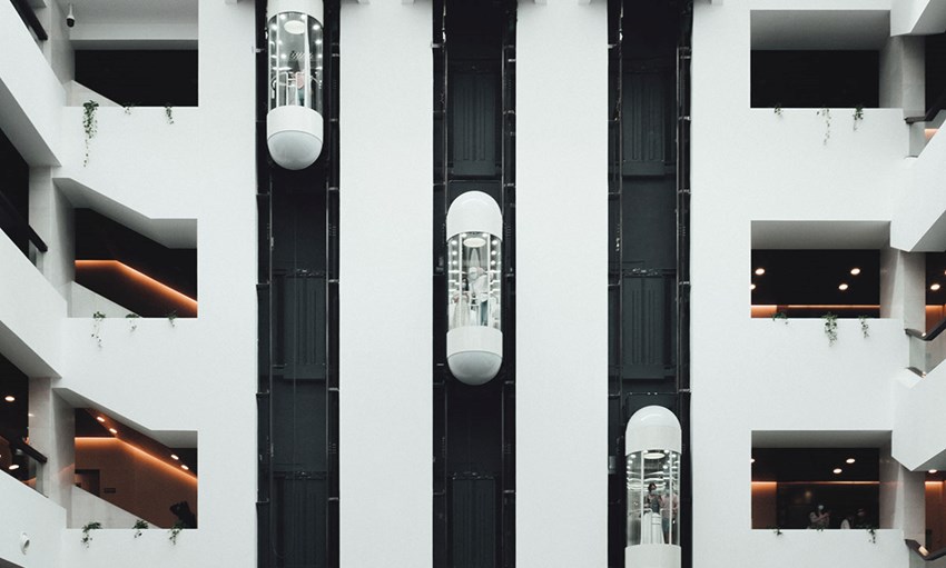 Modern elevator system in a white building with plants handing over the balisters